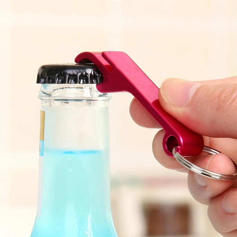 A red aluminum alloy Flesopener keyring bottle opener being used to open a glass bottle with a black cap containing blue liquid.