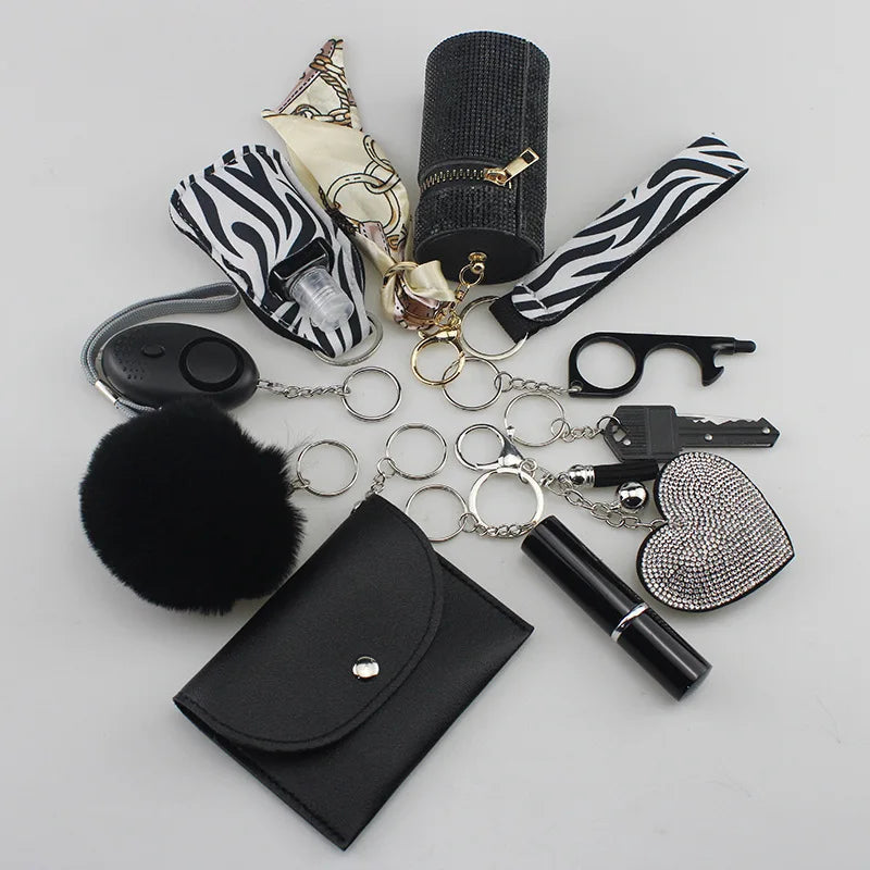 A collection of accessories from the "SafetyKey set" including a personal alarm, cardholder, wrist strap, lipstick holder, perfume bottle, organizer case, fluffy pompon, whistle, and various keychains, all displayed on a gray surface.