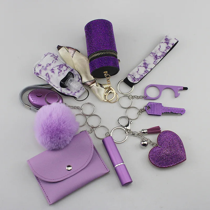 Purple SafetyKey set including a personal alarm, card holder, wrist strap, lipstick holder, perfume bottles, organizer bag, pompom, whistle, tactical tool, and heart-shaped keychain.