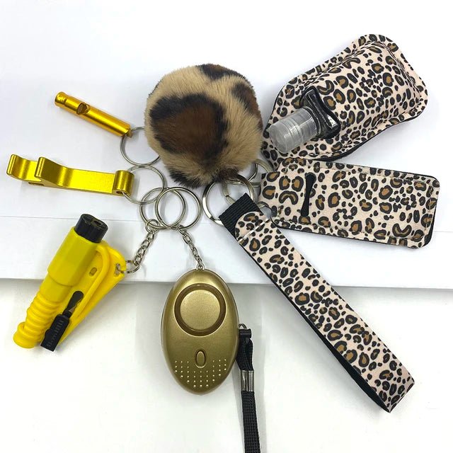 Elegant SafetyKey set 8-delig with gold and leopard print accessories including self-defense tools, a pom-pom, a personal alarm, and a sanitizer holder.