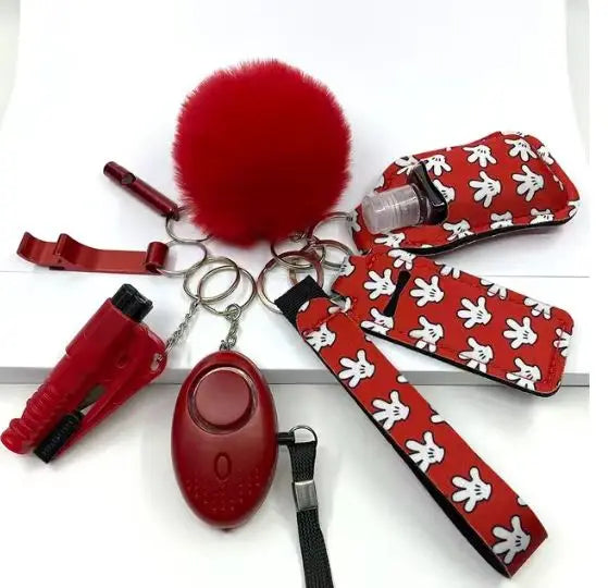 8-piece SafetyKey set featuring a personal alarm with LED light, whistle, bottle protector sleeve, two lipstick holders, bottle opener, no-touch door opener, red fluffy Pompon ball, and wrist strap with red and white cartoon glove pattern.