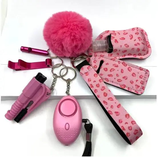 Pink SafetyKey set 8-delig including a personal alarm with LED light, a whistle, a protective bottle cover, two lipstick pouches, a bottle opener, a no-touch door opener, a fluffy pom-pom keychain, and an easy-to-carry wrist strap.