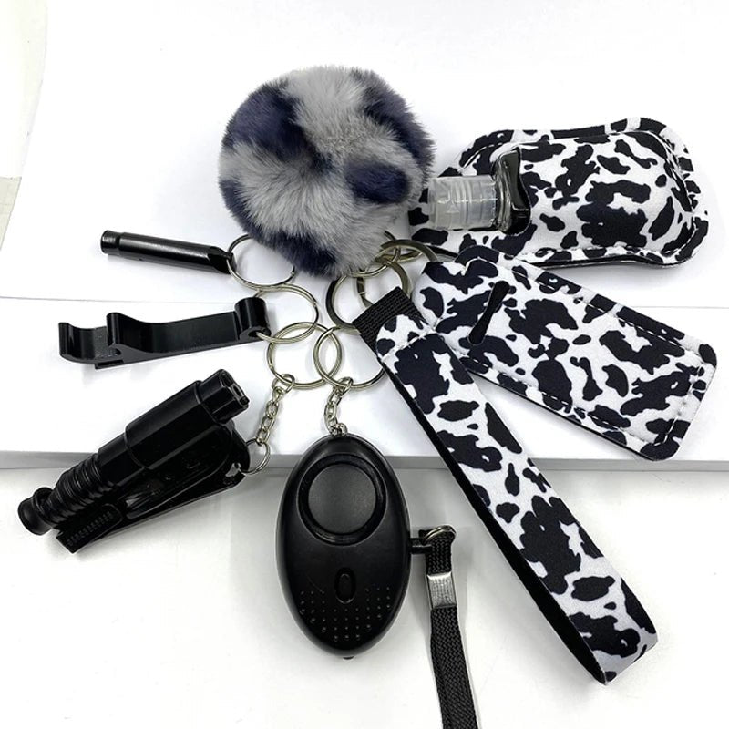 A set of eight black and white self-defense safety tools, including a furry keychain, a black alarm device, a cow print hand sanitizer holder, and various key rings.