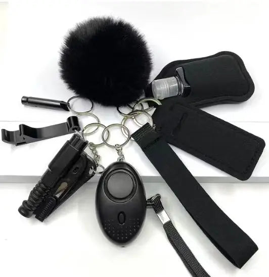 Eight-piece SafetyKey set featuring a personal alarm, LED light, whistle, bottle protection cover, two lipstick pouches, bottle opener, no-touch door opener, pom-pom keychain, and wrist strap for easy carrying.