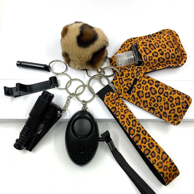 A set of eight safety keychain accessories, including a fur ball, black whistle, leopard-print hand sanitizer holder, black self-defense tool, black alarm, and leopard-print wrist strap, all connected by silver rings.