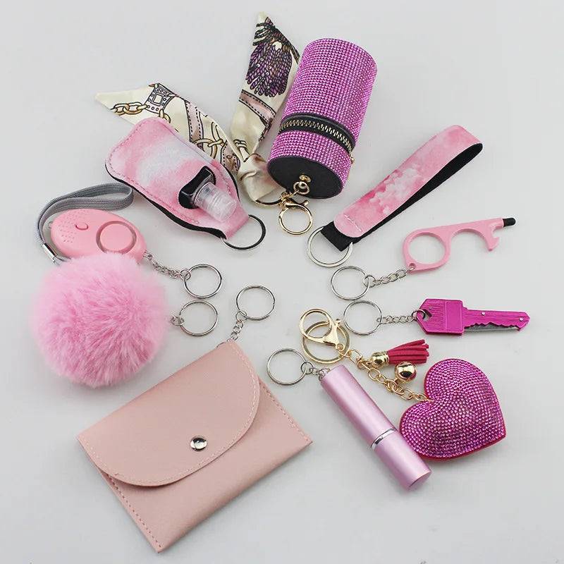 Set of personal safety items including a pink siren alarm, cardholder, pink pompon, polka-dot and satin wrist straps, lipstick holder, pink perfume bottle, organizer pouch, and a purple glittery heart keychain.